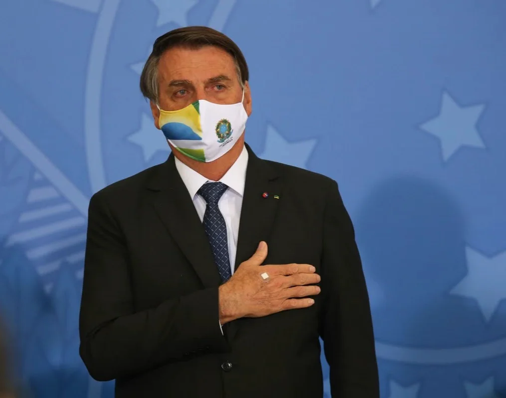 Jair Bolsonaro de máscara, com a mão no peito