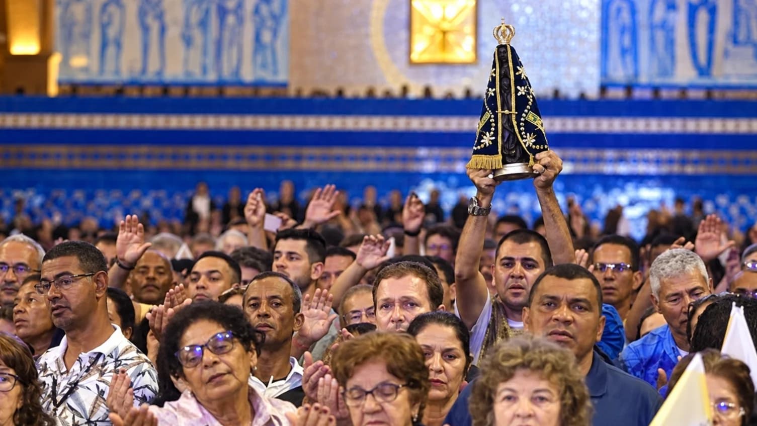 Fiéis rezam no Santuário Nacional de Aparecida enquanto um homem ergue a imagem de Nossa Senhora Aparecida