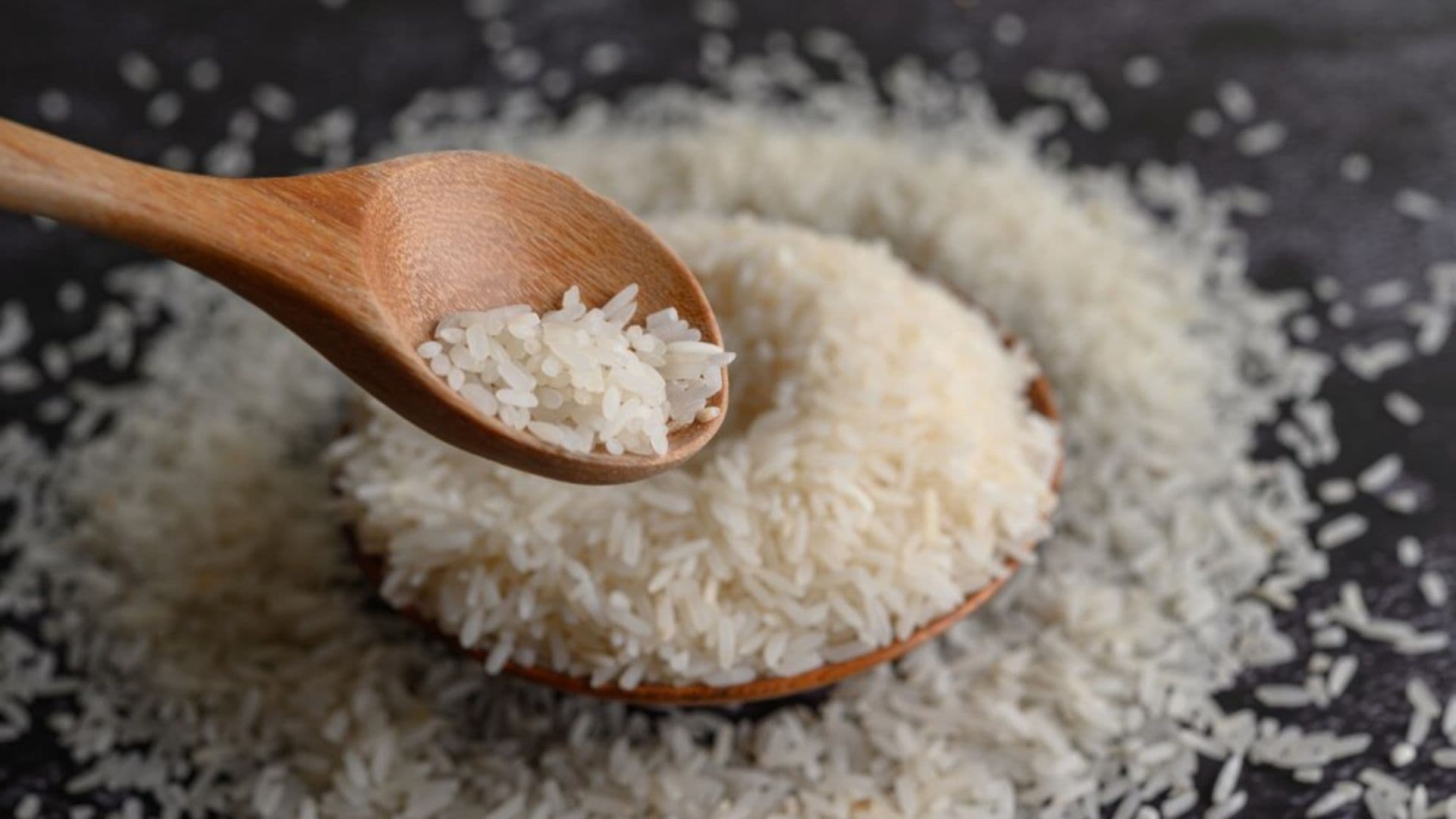 Arroz espalhado em superfície preta é recolhido com colher de madeira