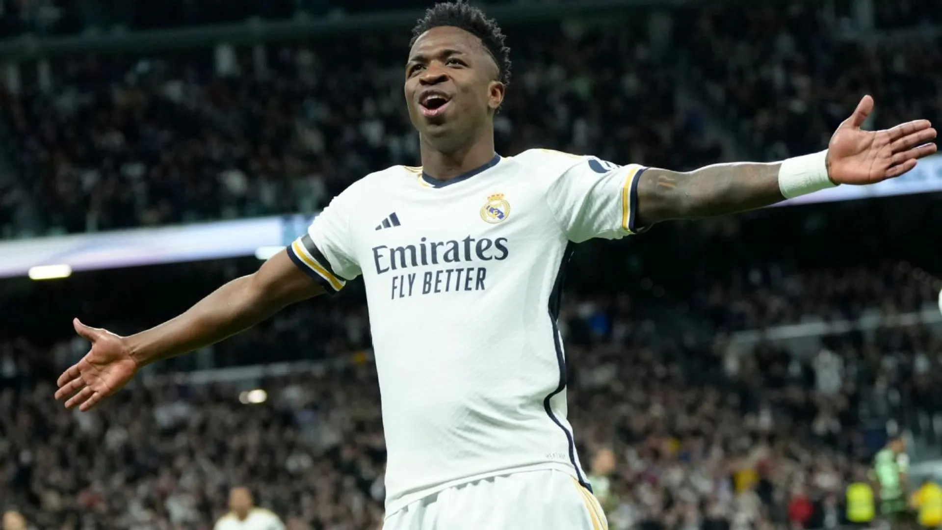 Vini Jr. de braços abertos em meio a um jogo.