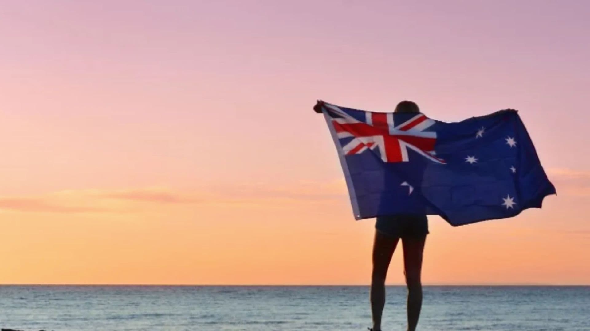 Austrália proíbe menores de 16 anos nas redes sociais. Homem aparece segurando a bandeira da Austrália e olhando o mar
