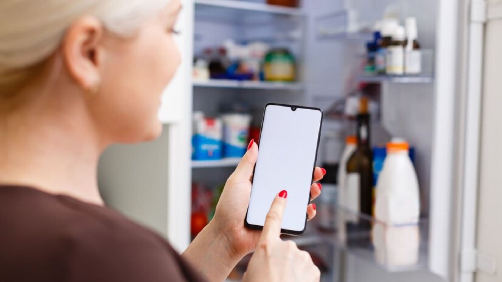 Mulher usa celular perto de uma geladeira aberta IBGE: celulares superam geladeiras entre os pobres