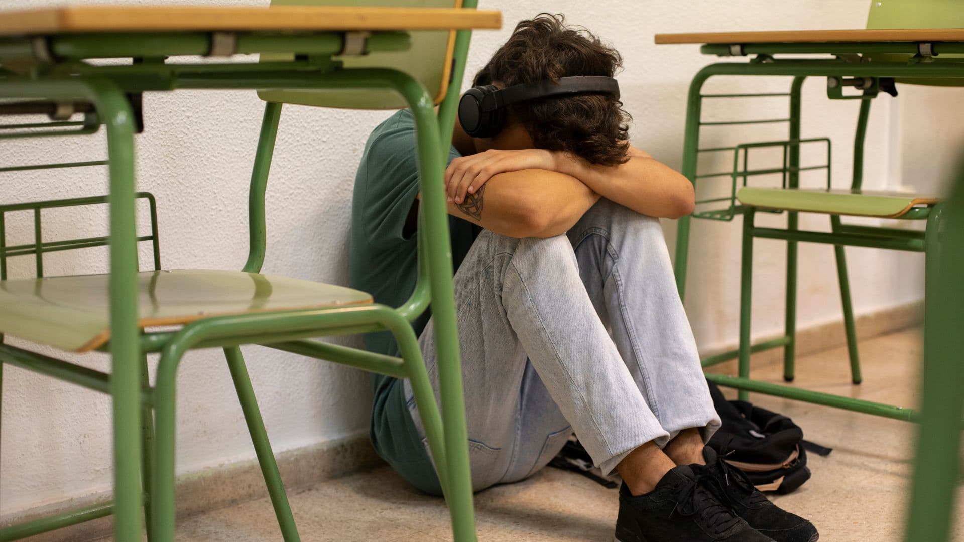 Foto de jovem de cabeça baixa ao lado de uma carteira. Ele está sentado no chão. IBGE: 1 em Cada 5 Jovens Não Termina a Educação Básica