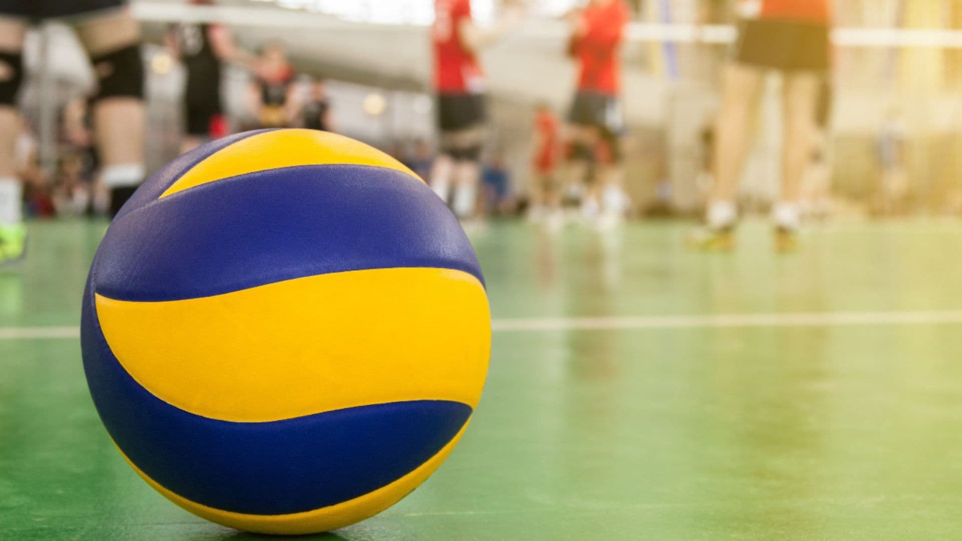Bola de vôlei amarela e azul aparece no chão de quadra. Universidade é processada por atleta trans em time feminino