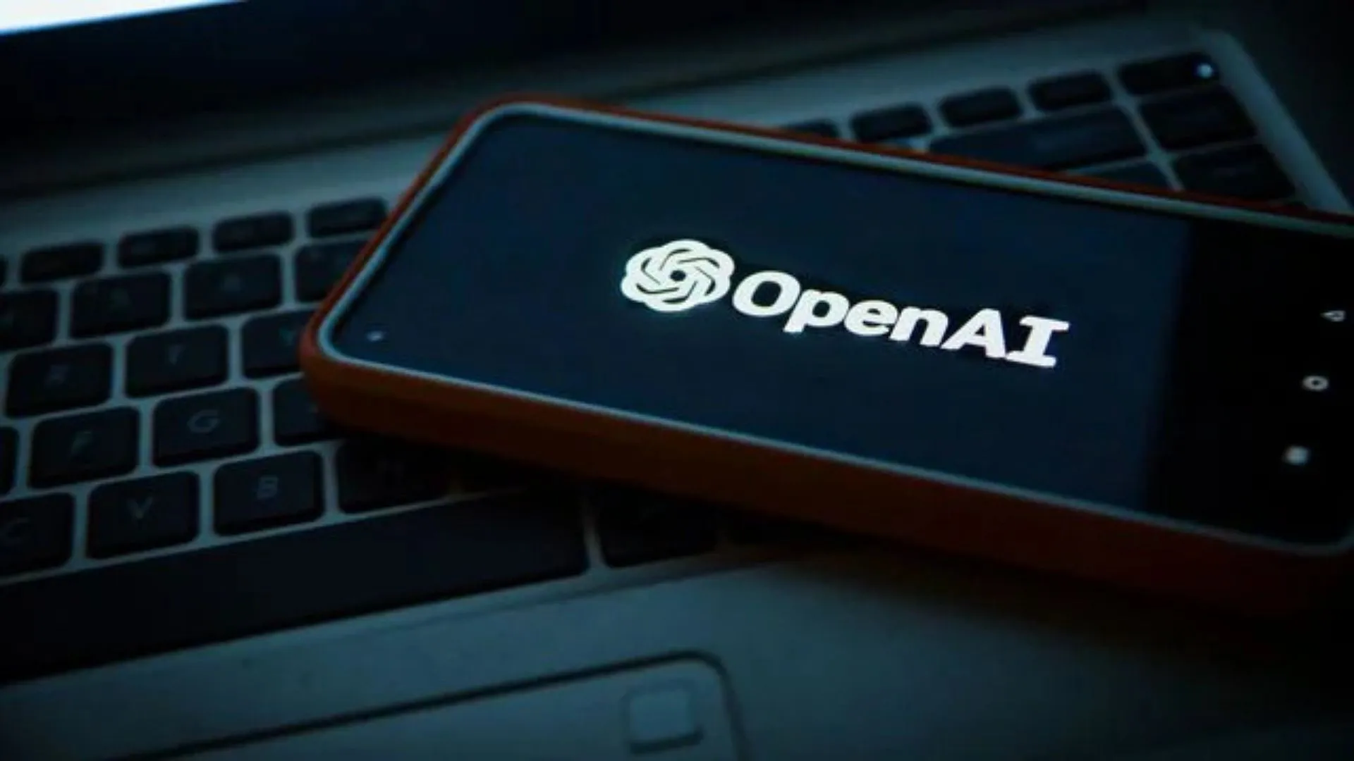 celular com tela abrindo OpenAI e um teclado de computador em frente