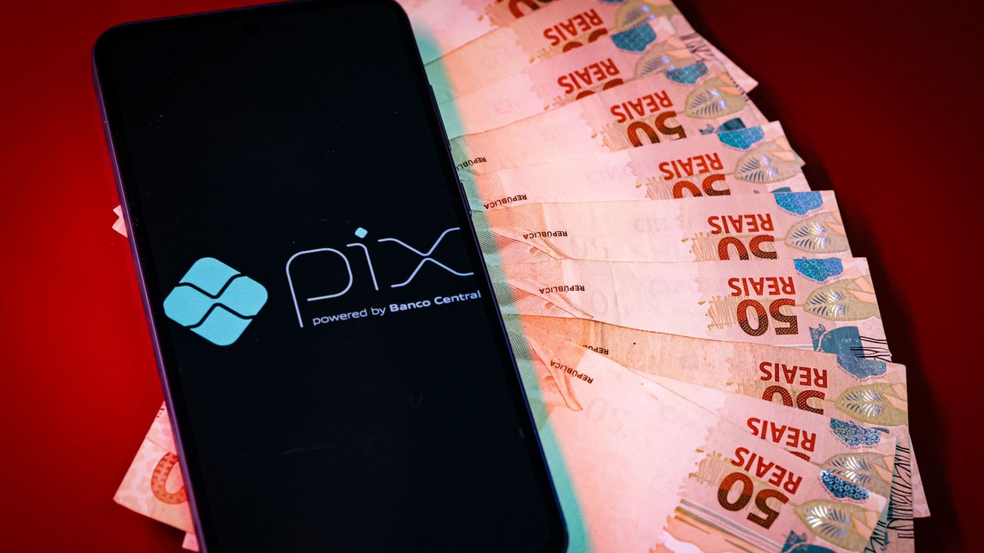 Um celular com o PIX aberto em cima de um maço de notas de 10 reais.
