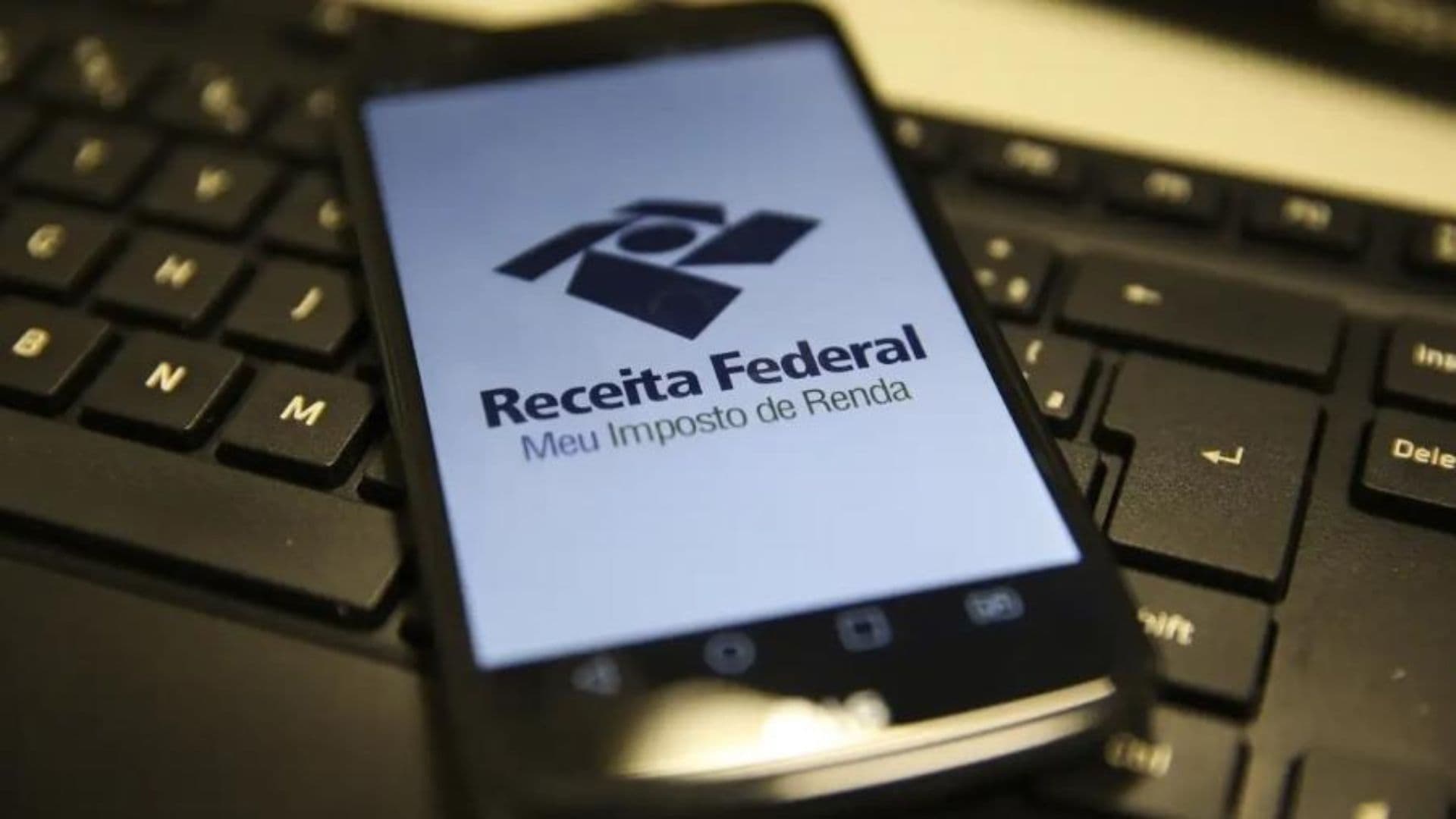 Celular aberto no aplicativo da Receita Federal em cima de um teclado. Começou o prazo para a declaração dos ganhos de 2024.