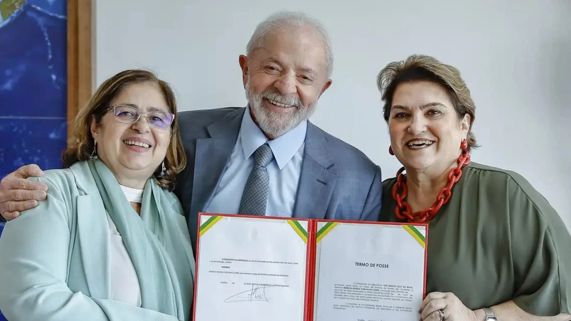Presidente Lula abraçado com Cida Gonçalves e Márcia Lopes enquanto seguram o termo de posse da nova ministra