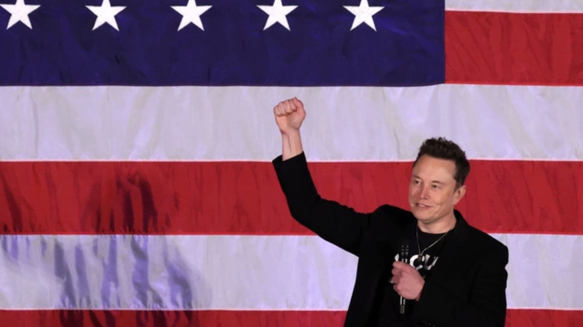 Elon Musk discursando em frente a uma bandeira americana.