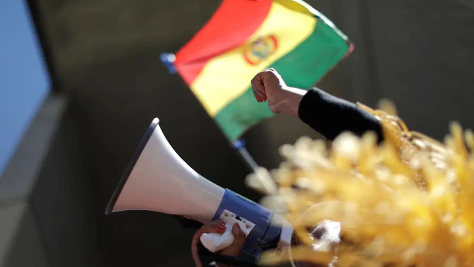 Pessoa falando em um auto-falante segurando a bandeira da Bolívia durante época das eleições.