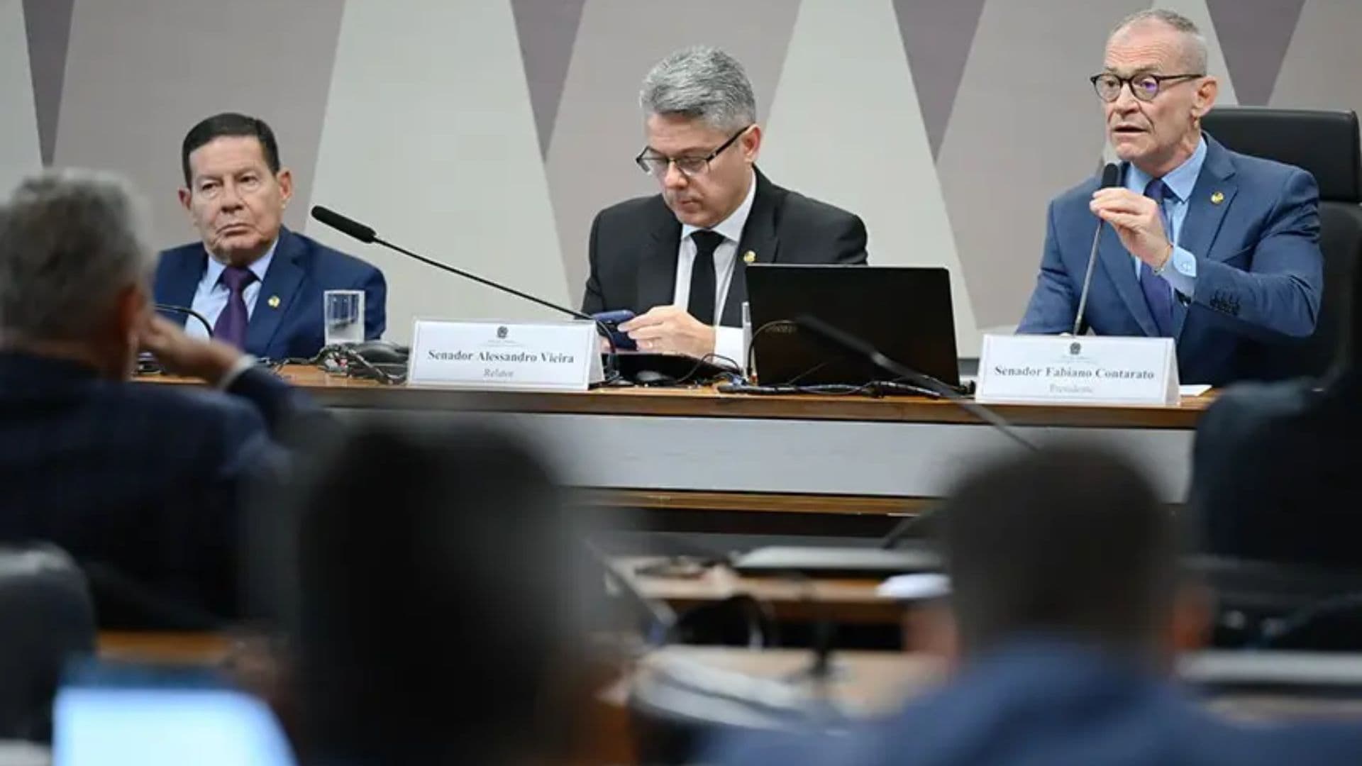 Os senadores Hamilton Mourão, Alessandro Vieira e Fabiano Contarato sentados à mesa durante uma sessão em comissão no Senado Federal.
