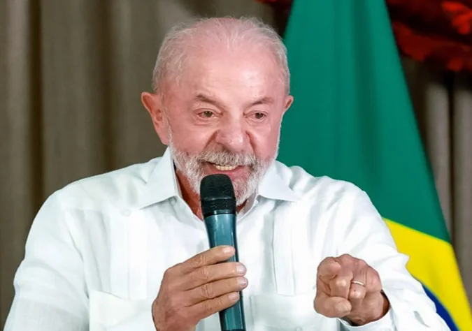Lula fala ao microfone diante da bandeira do Brasil