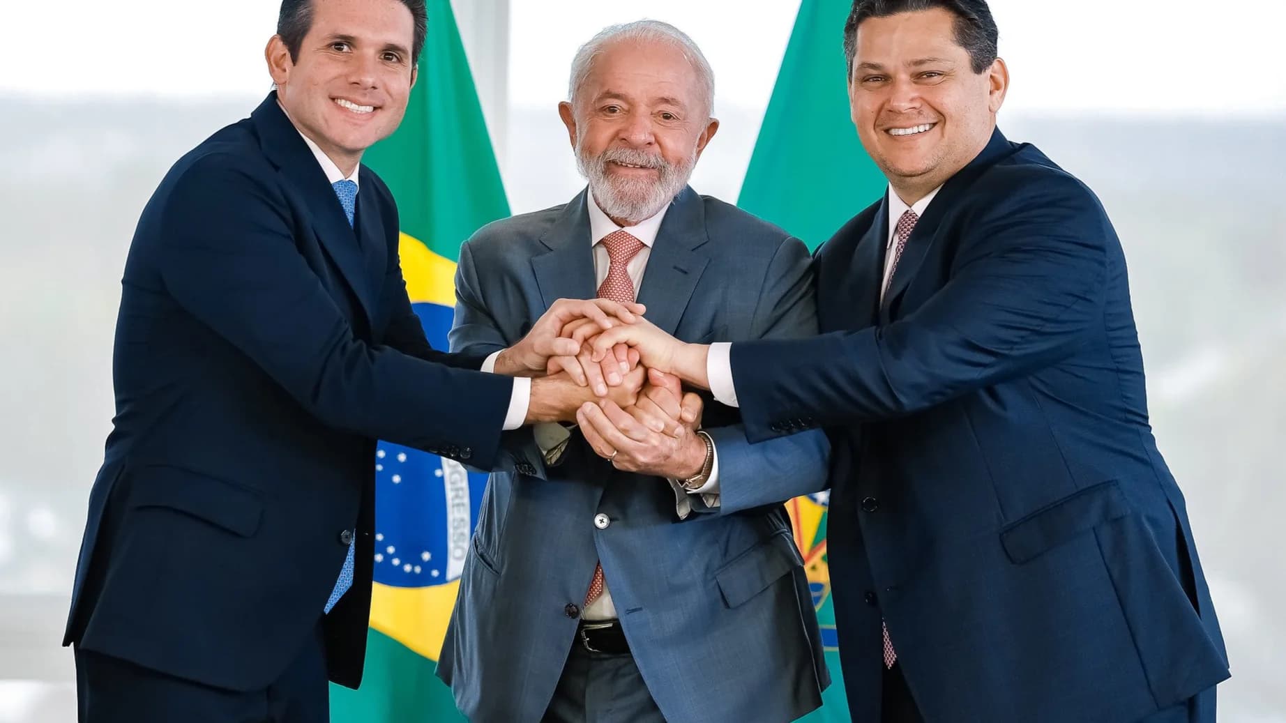 Lula e os presidentes da Câmara e do Senado unem as mãos diante de bandeiras