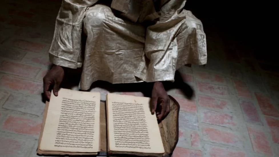 Homem segura manuscrito antigo aberto sobre o chão